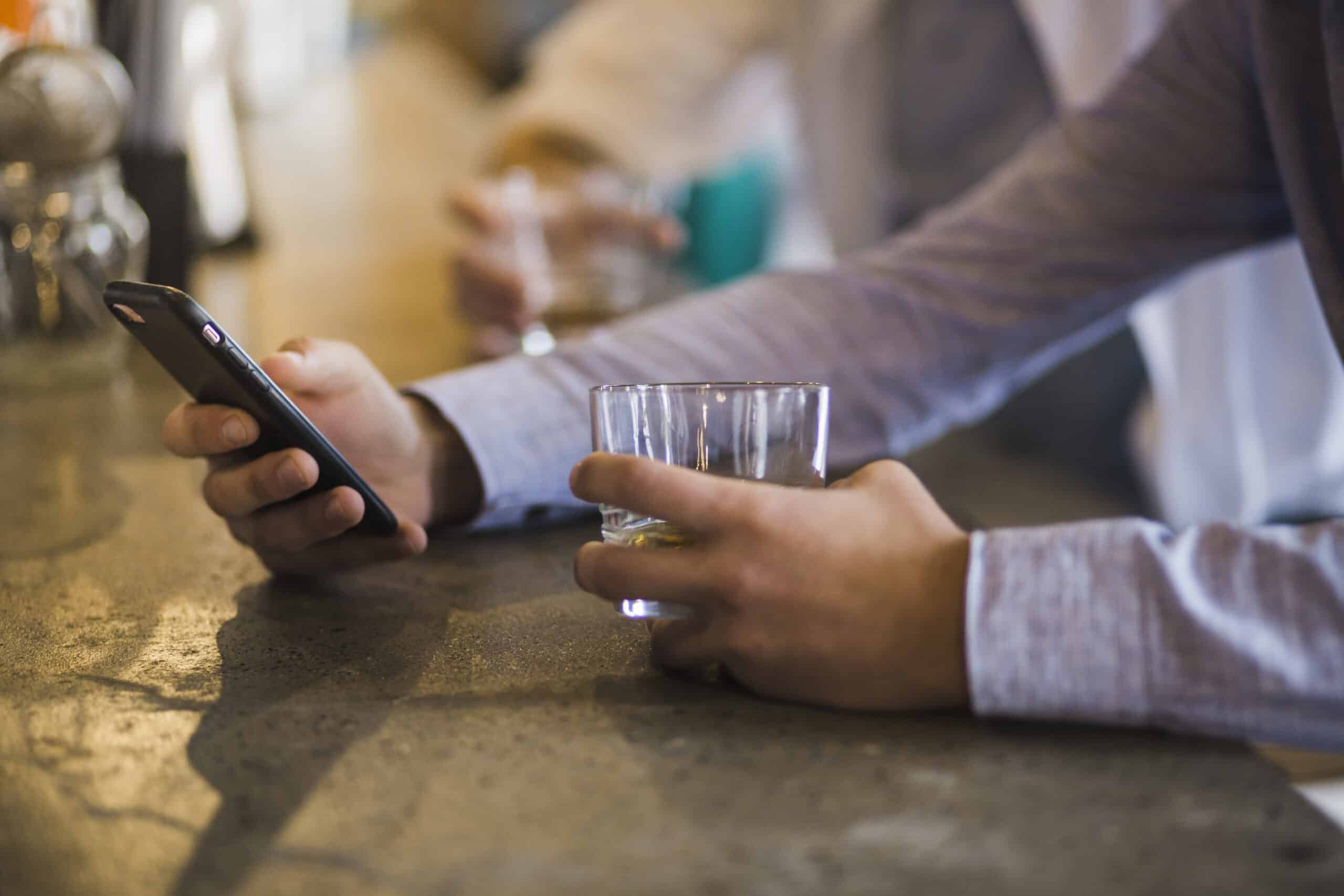 Pub customer using mobile phone while holding a drink, connected to pub WiFi